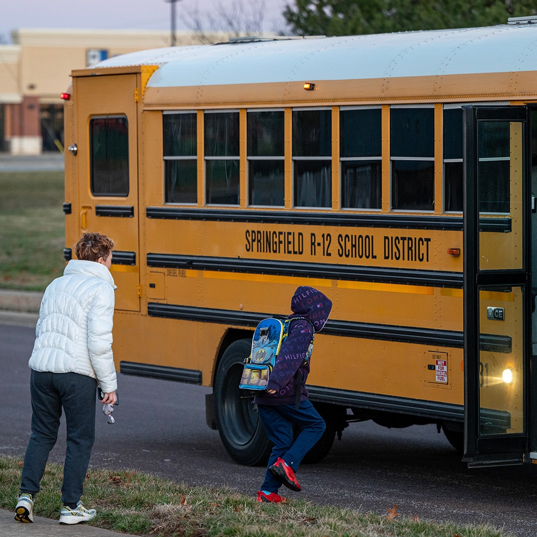 A mother watches her child board a yellow school bus
