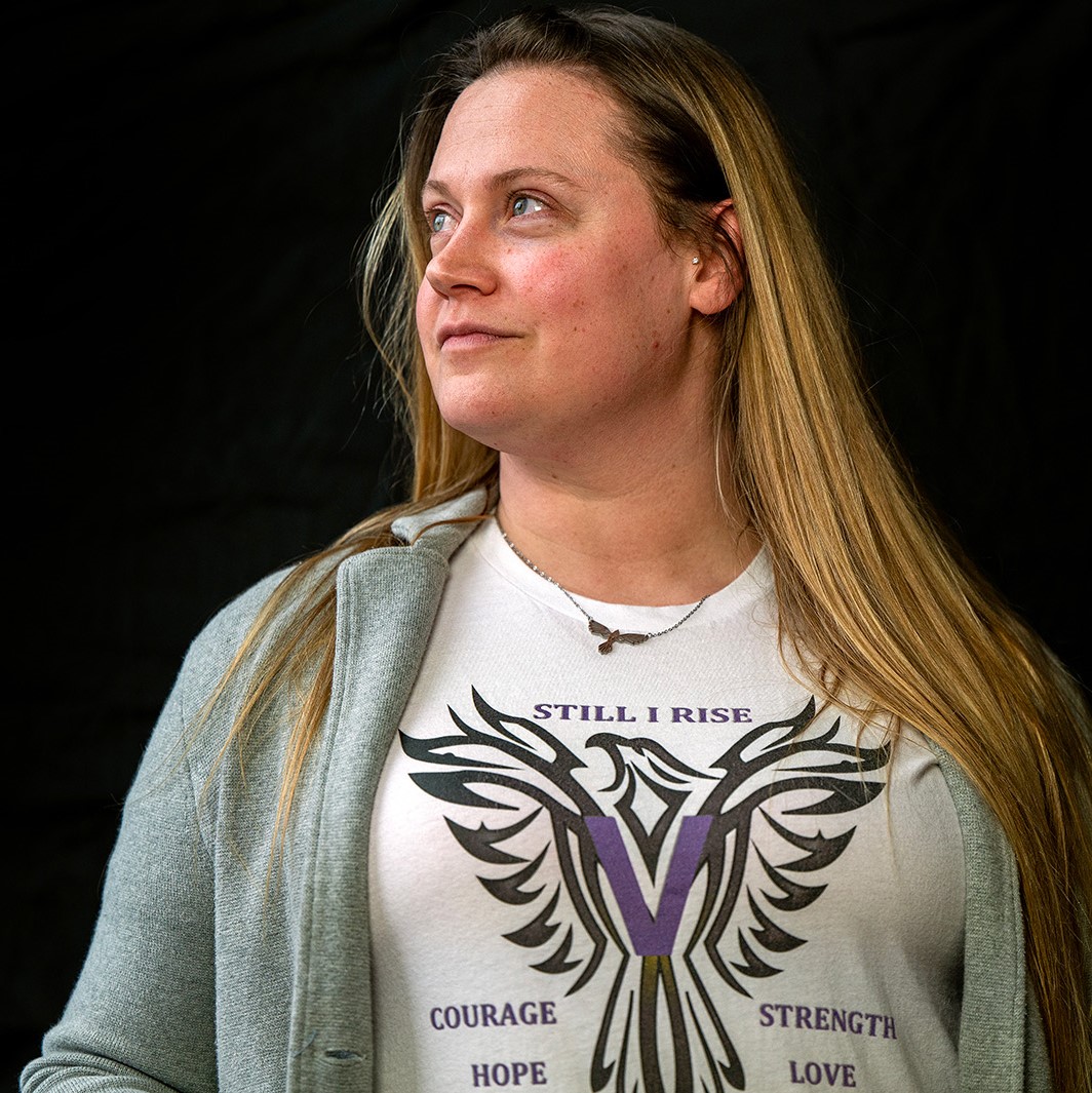 A woman wearing a shirt that says "Still I rise" poses in front of a black backdrop
