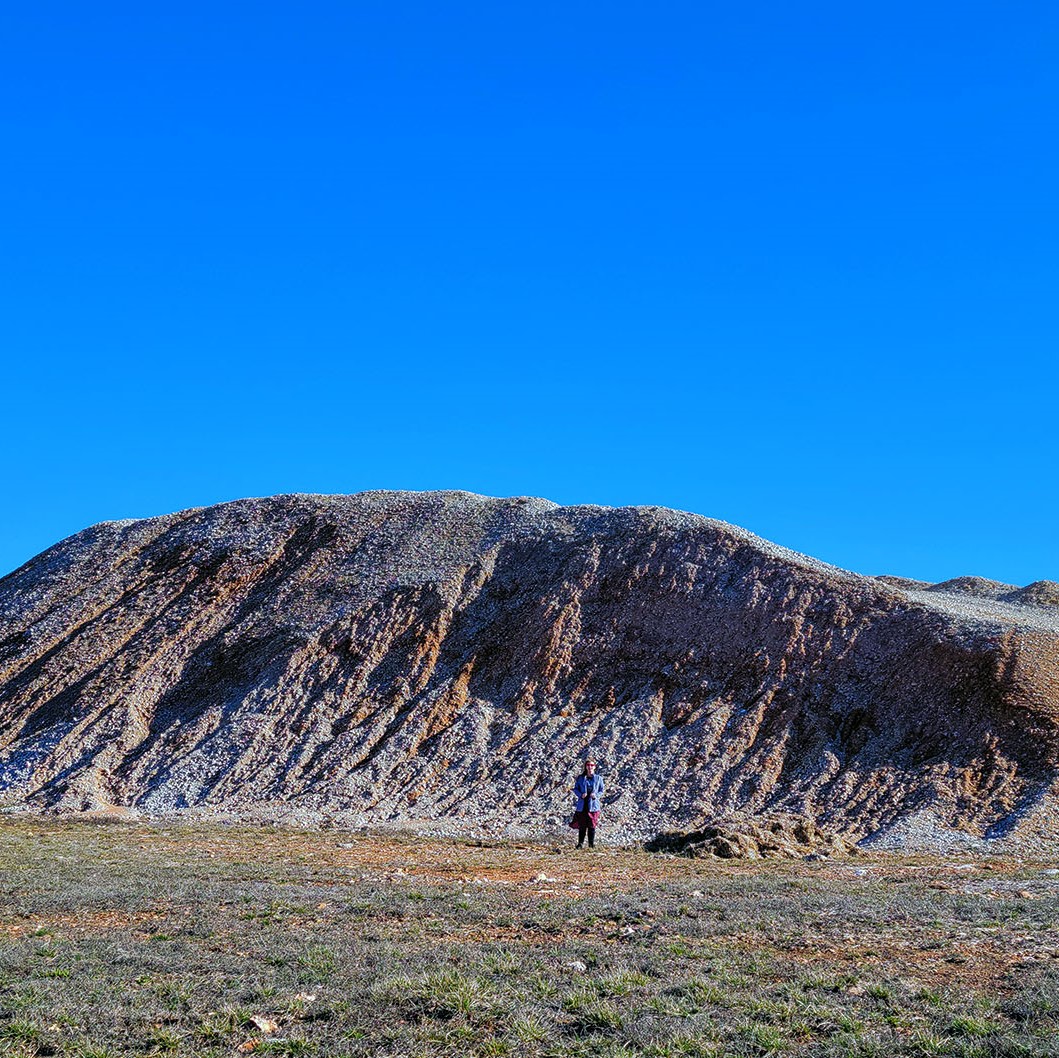 A woman stands in front of a 20-foot-tall pile of rocks