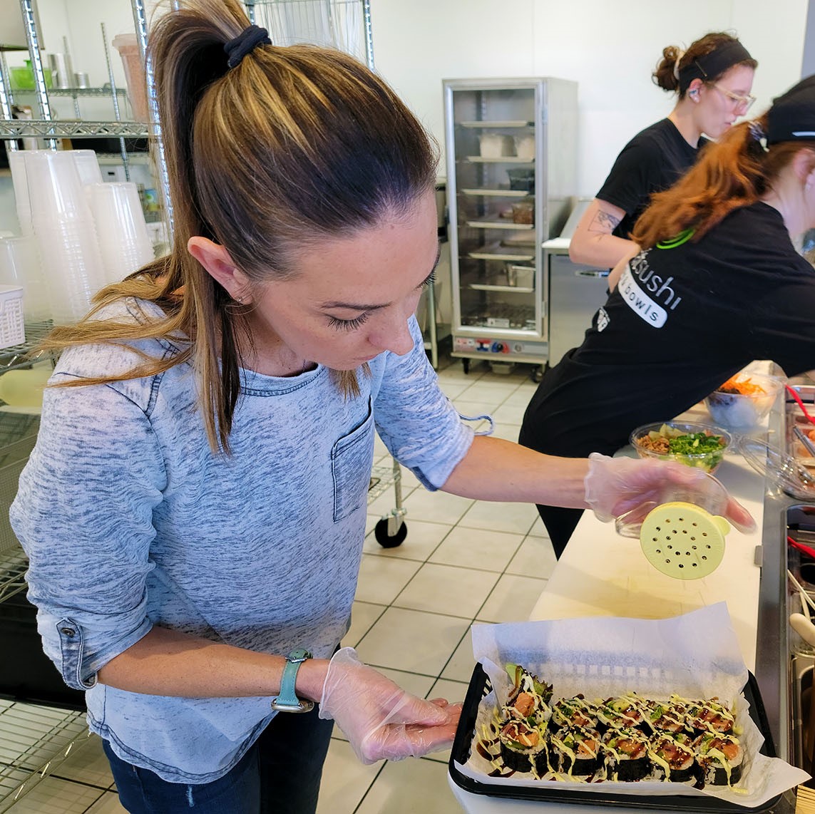 A woman in a restaurant kitchen prepares a sushi roll