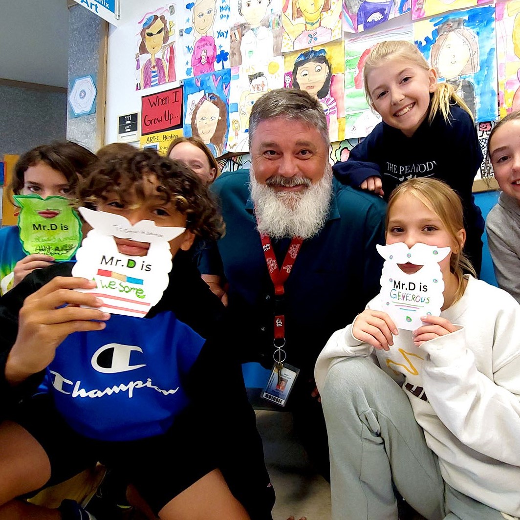 A teacher is surrounded by students holding up fake beards that look like his