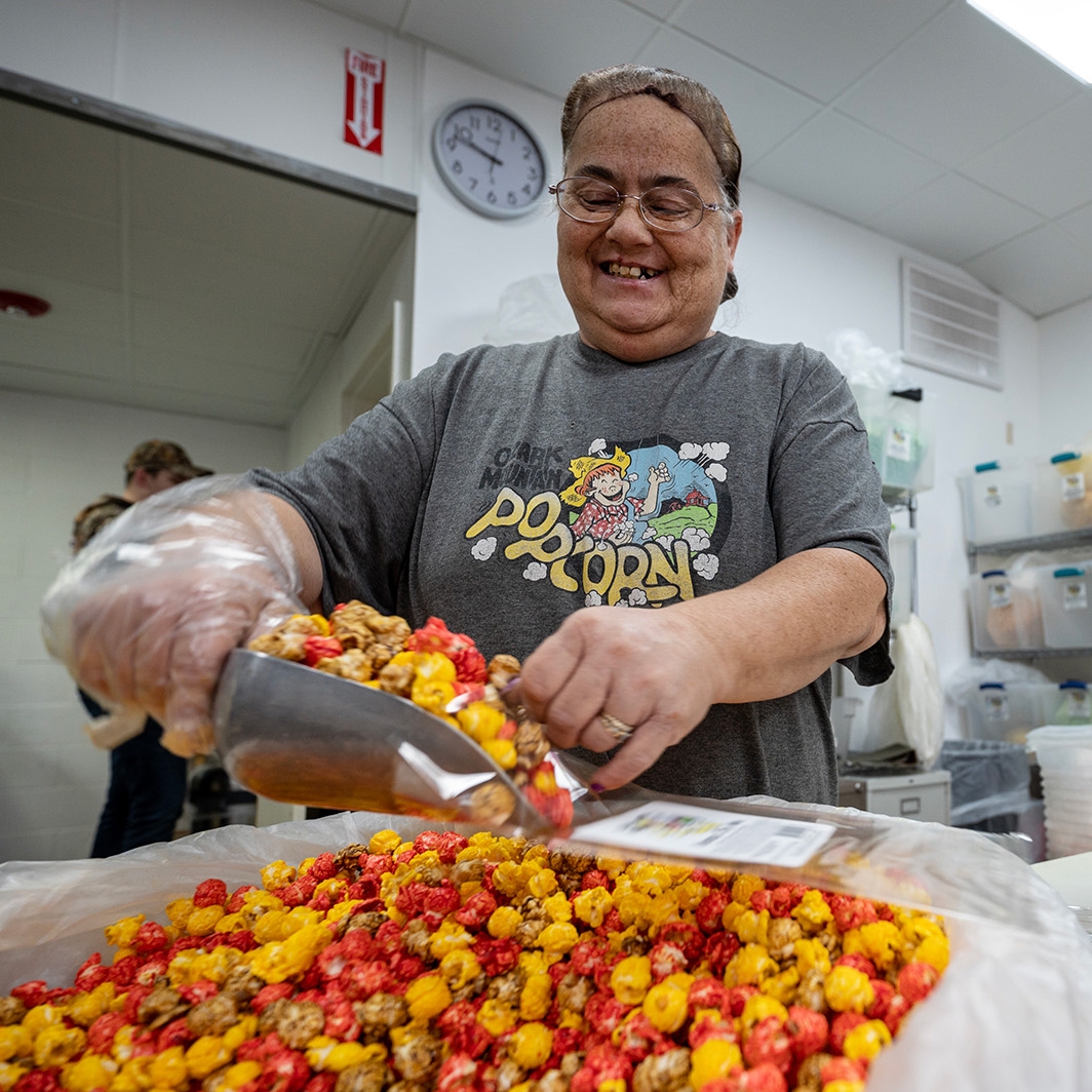 A woman scoops red and yellow popcorn into a clear bag