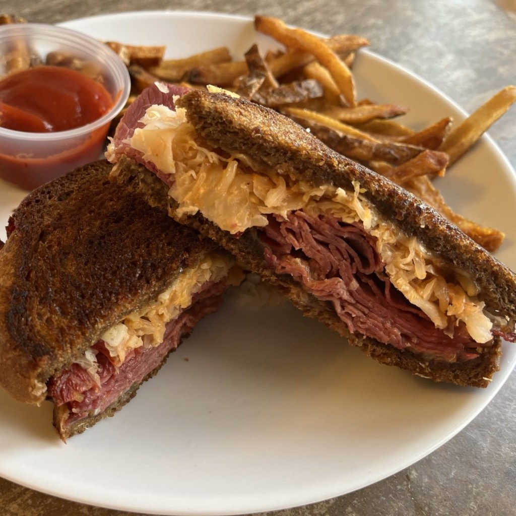 A Reuben sandwich and french fires sit on a white plate