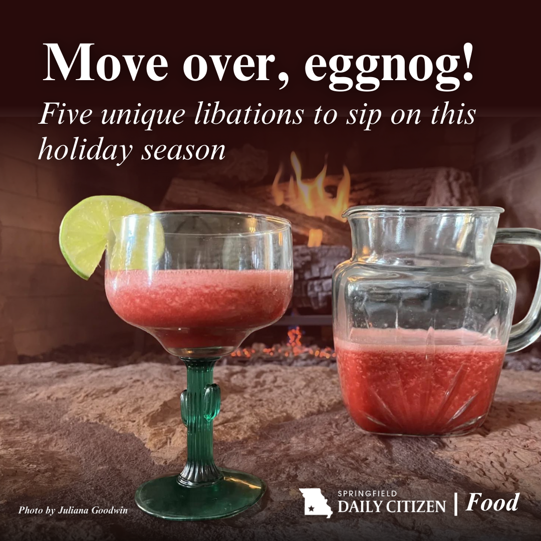 A cranberry margarita, garnished with a lime wheel, sits next to a pitcher on the hearth of a fireplace. A fire can be seen in the background. Text on the image reads: "Move over, eggnog! Five unique libations to sip on this holiday season." (Photo by Juliana Goodwin)