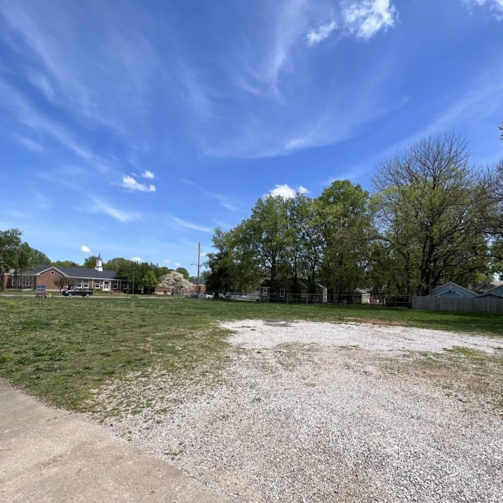 An empty lot with green grass and a gravel drive