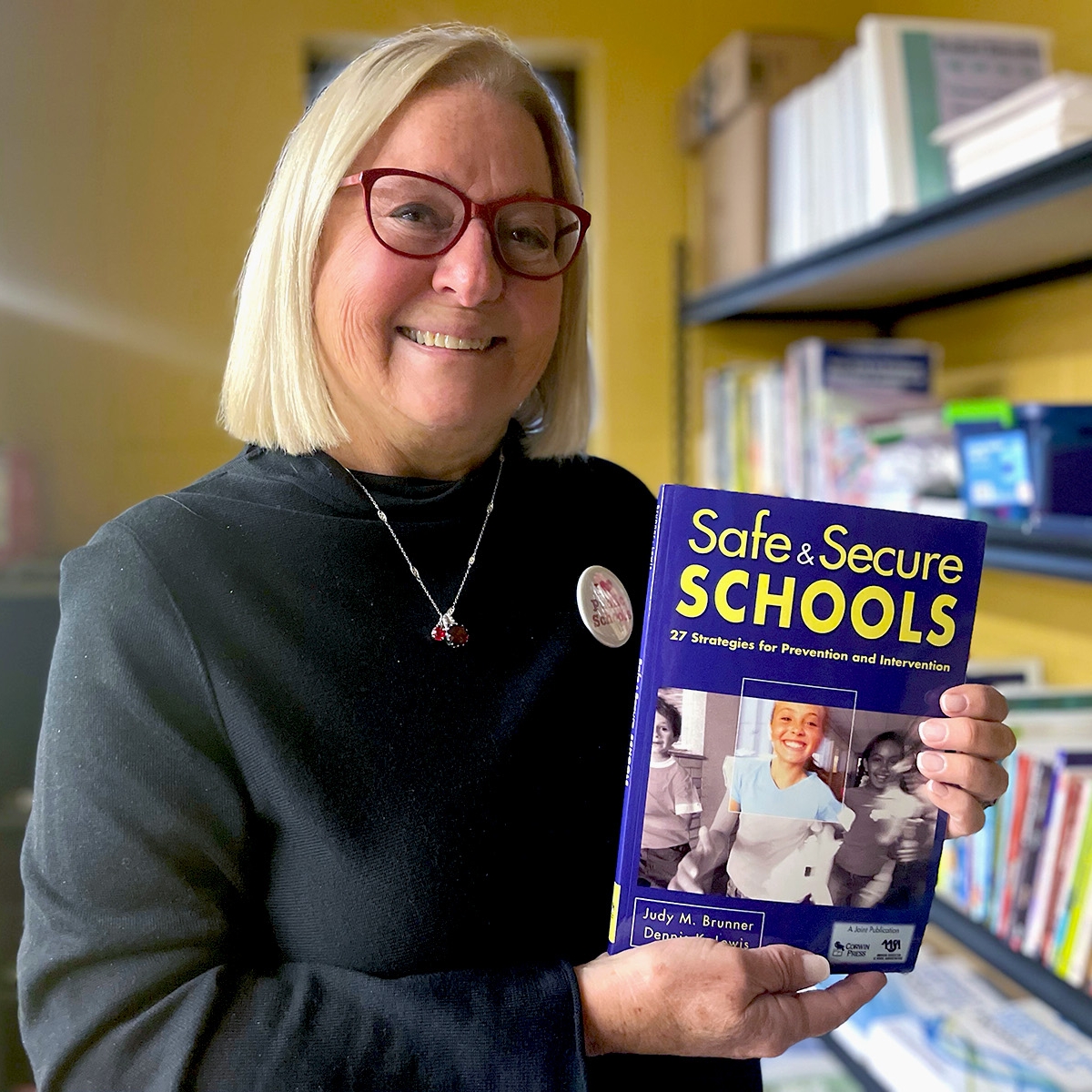 A woman holds a book titled "Safe & Secure Schools"