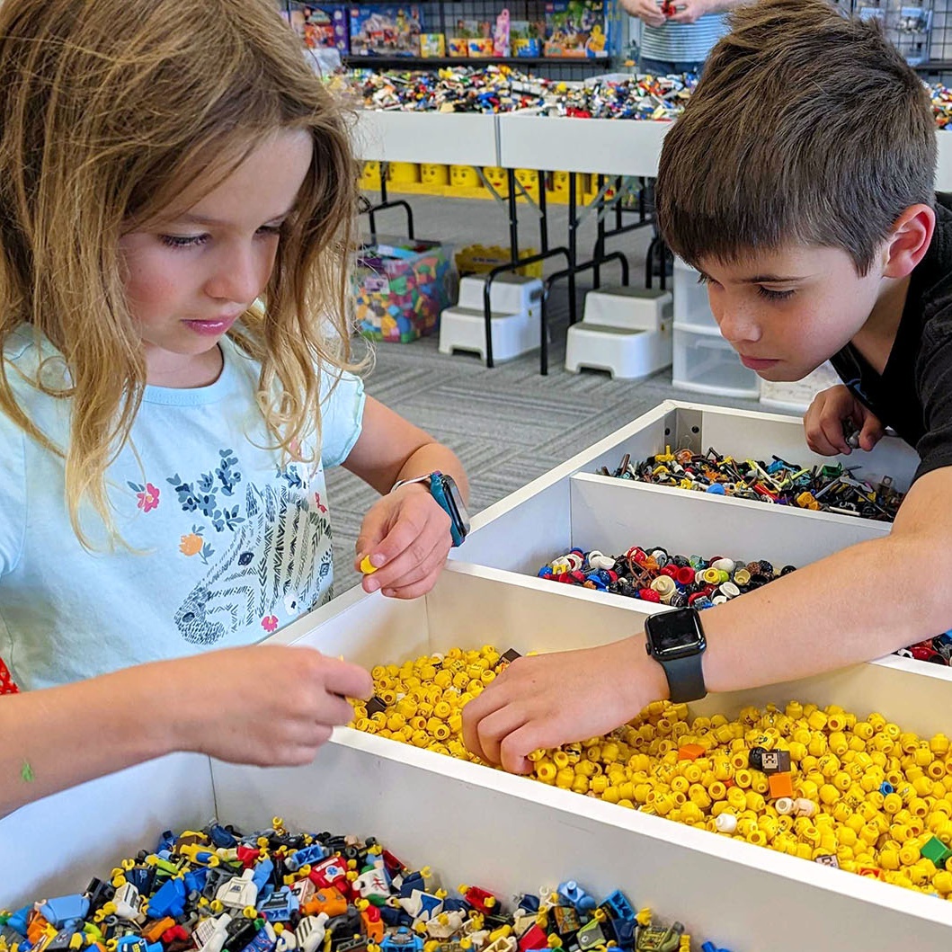 A boy and a girls look through trays of Lego bricks