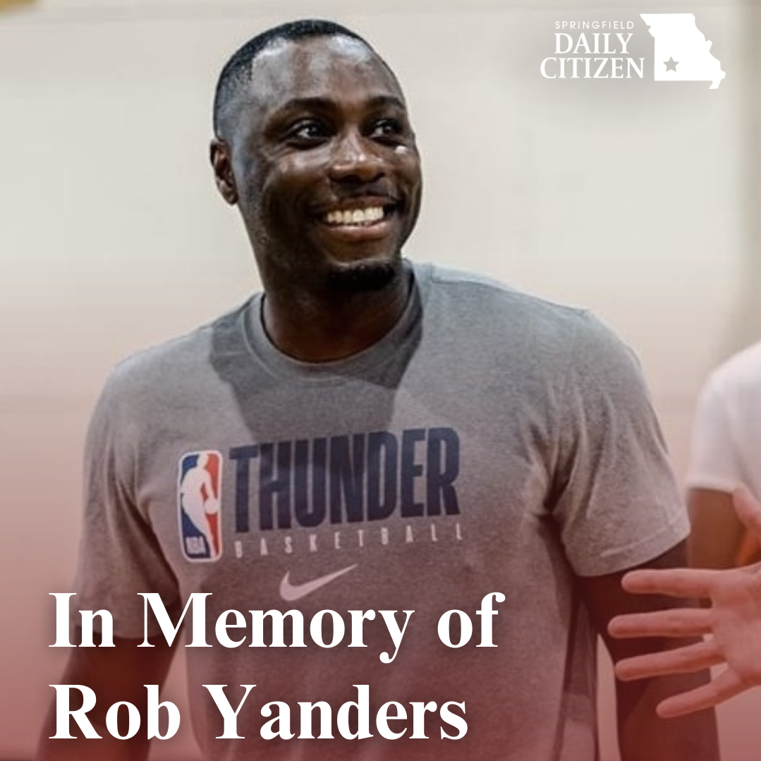 Rob Yanders, wearing a gray T-shirt reading "Thunder Basketball," smiles while coaching basketball players