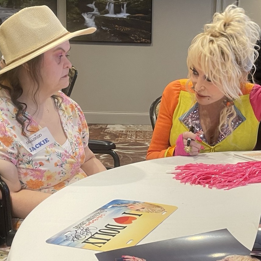 Country music legend Dolly Parton sits at a table, meeting a fan