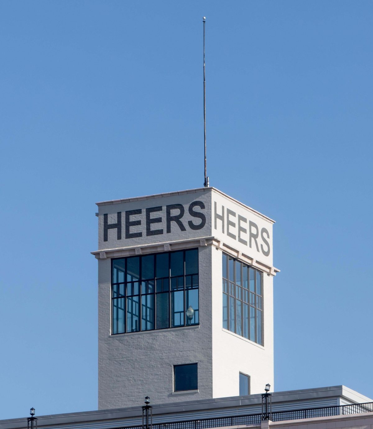 The tower of the Heers Building with a Blue Sky background. what seems to be a lightening antenna on top of the building.