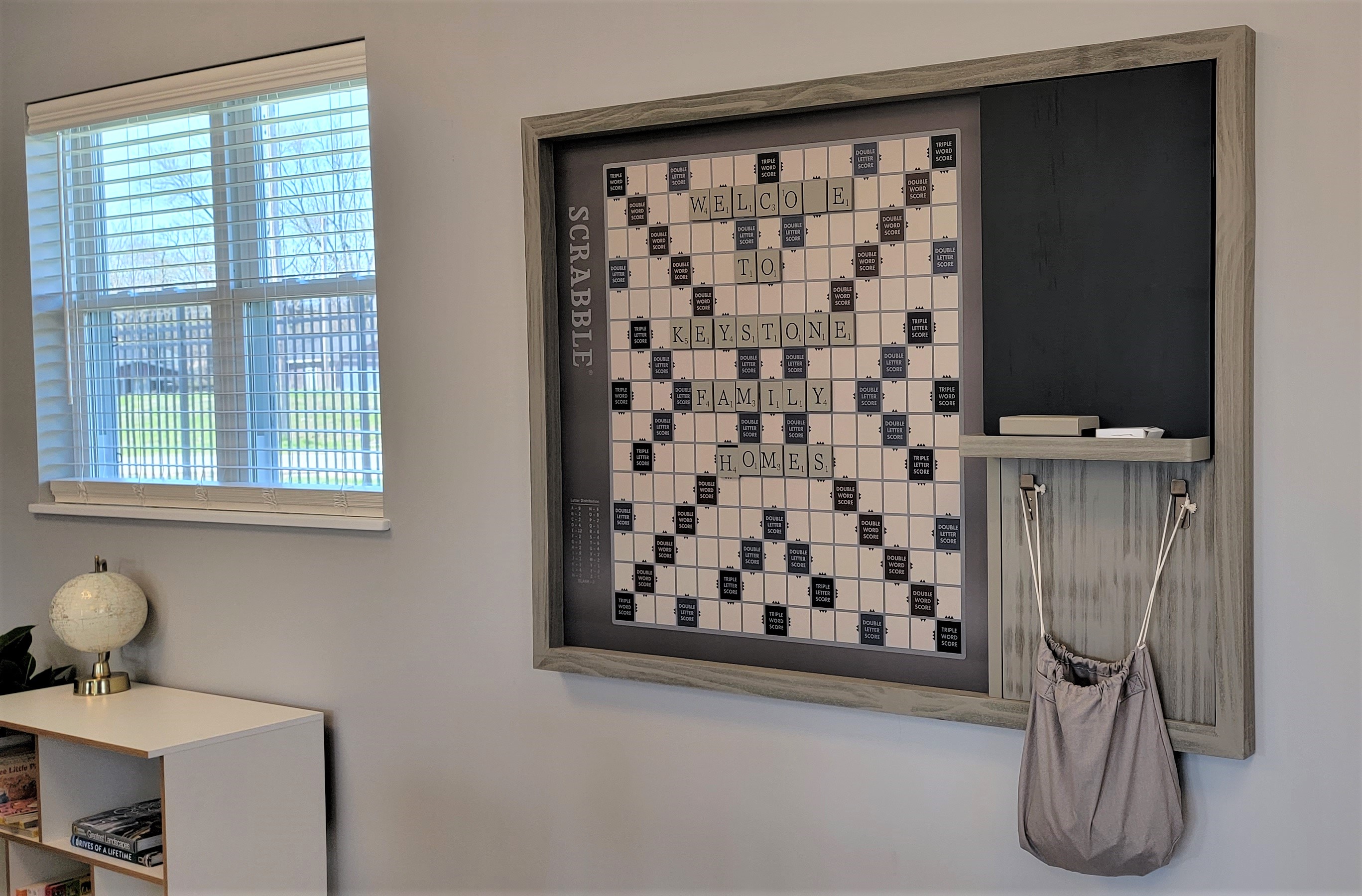 A decorative Scrabble Game is on the wall of the community room for residents. Light Gray walls with vertical game and chalk board.