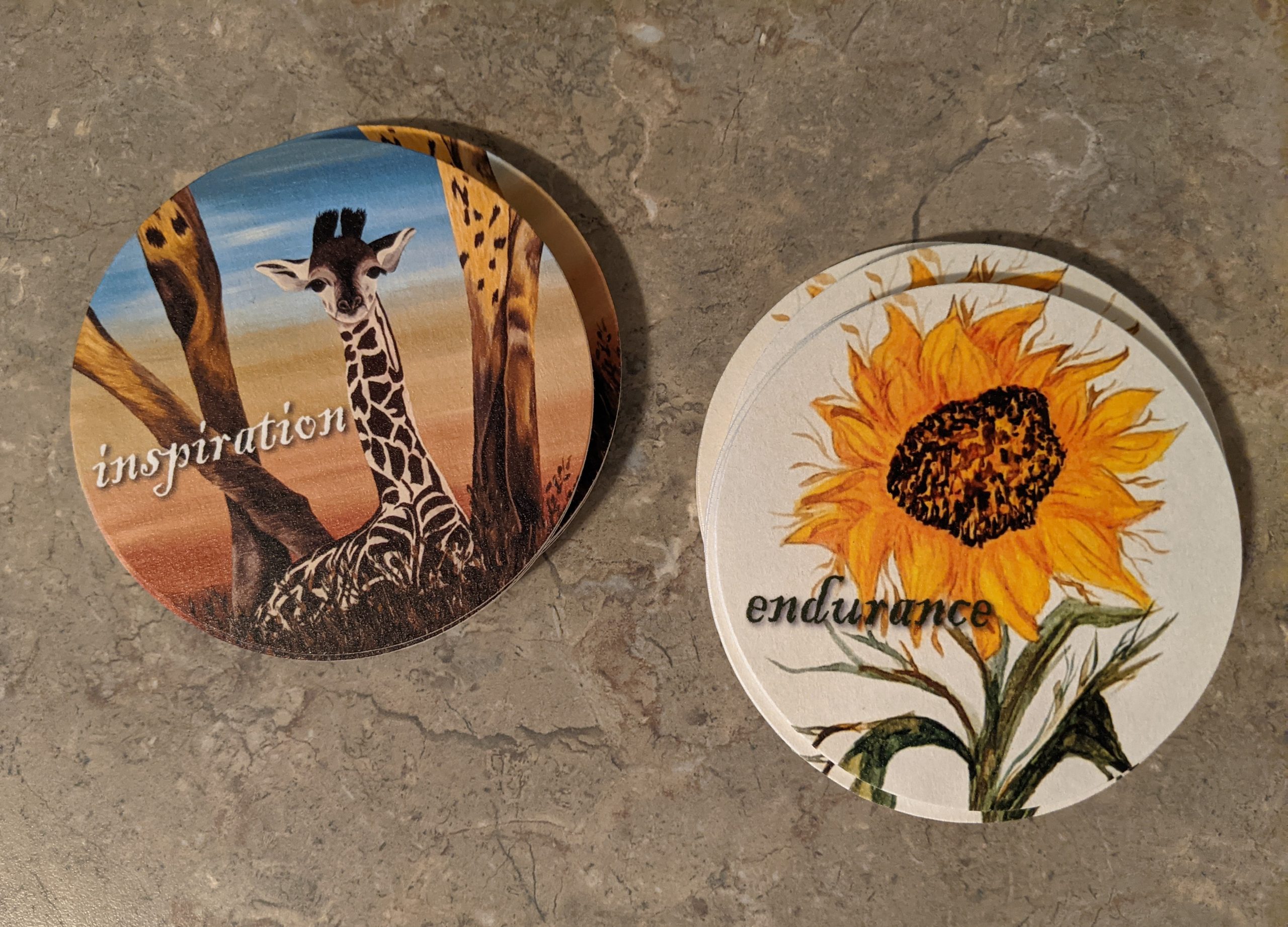 Two painted coasters, one with a giraffe and the other with a sunflower