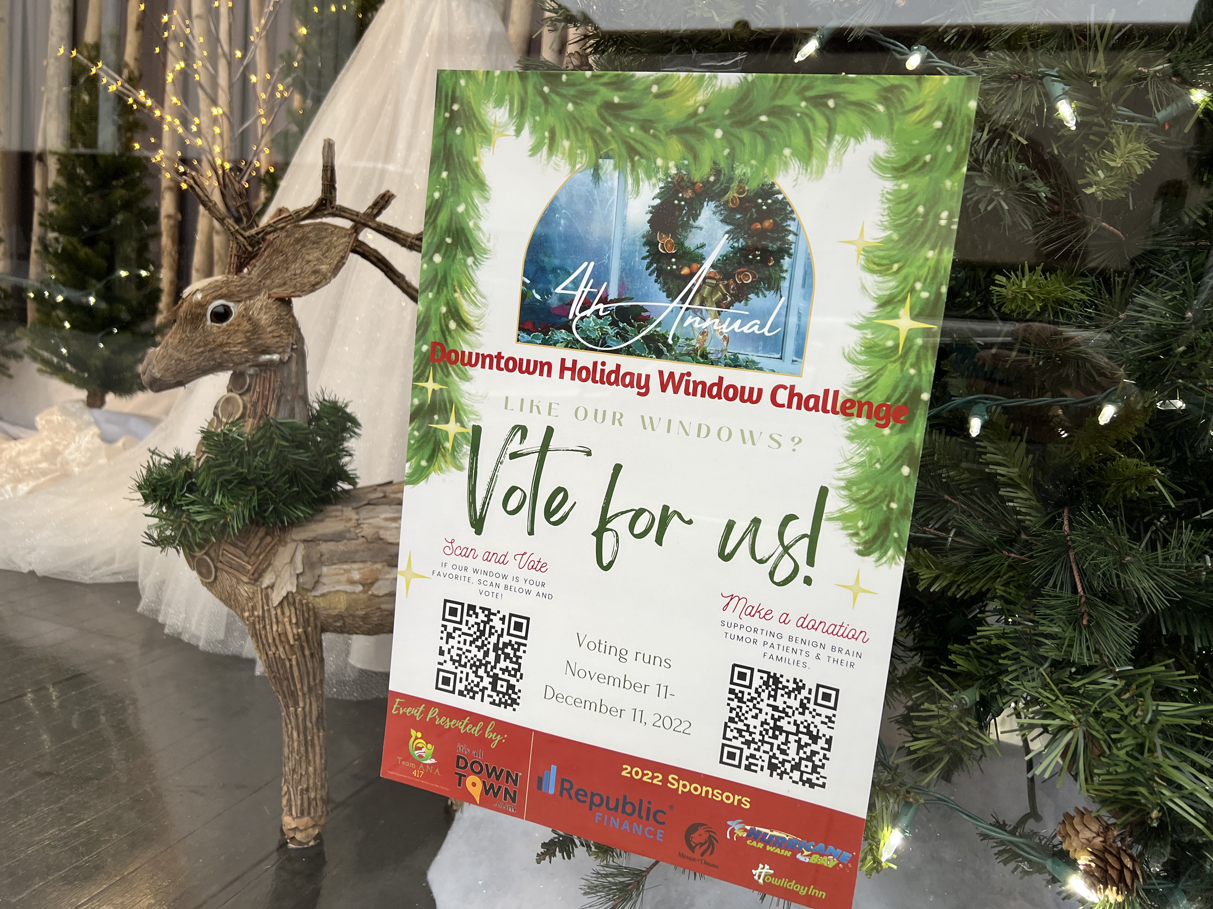A sign in a window encourages people to vote for this display in the Downtown Holiday Window Challenge