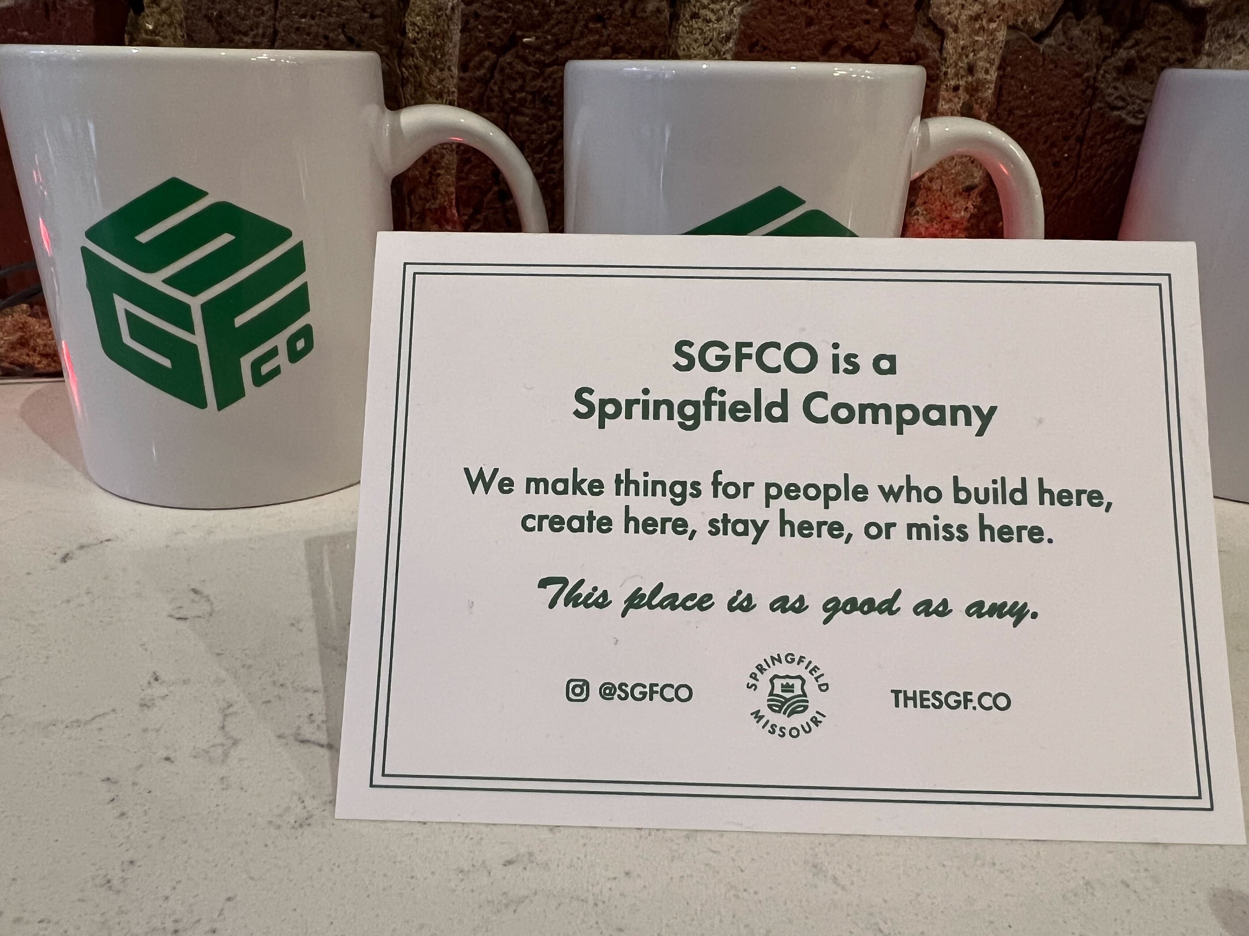 A white mug sits on a counter with a sign advertising SGFCO