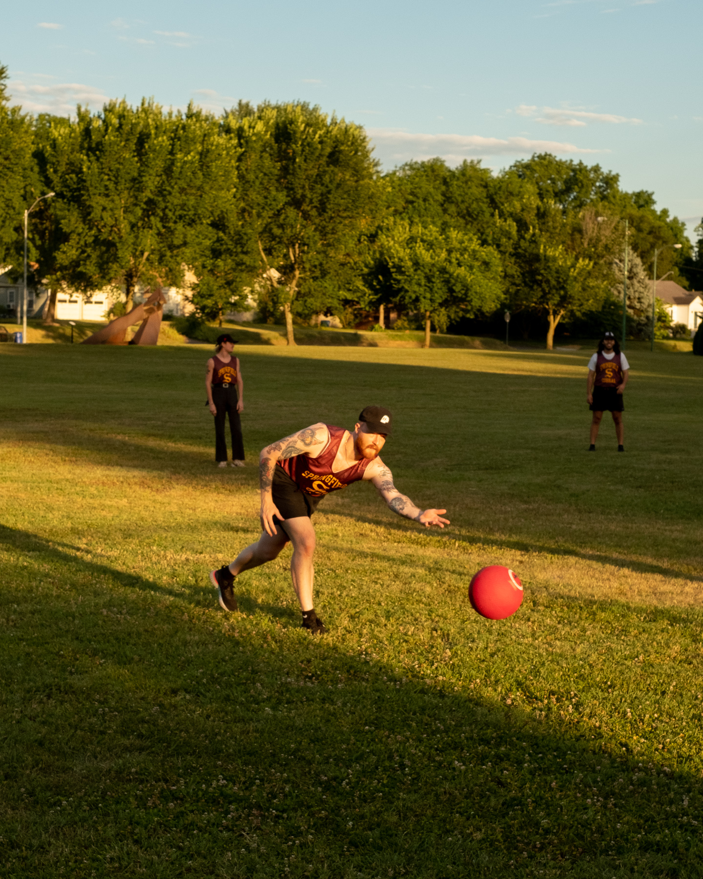 A player rolls a red rubber ball during a game of kickball