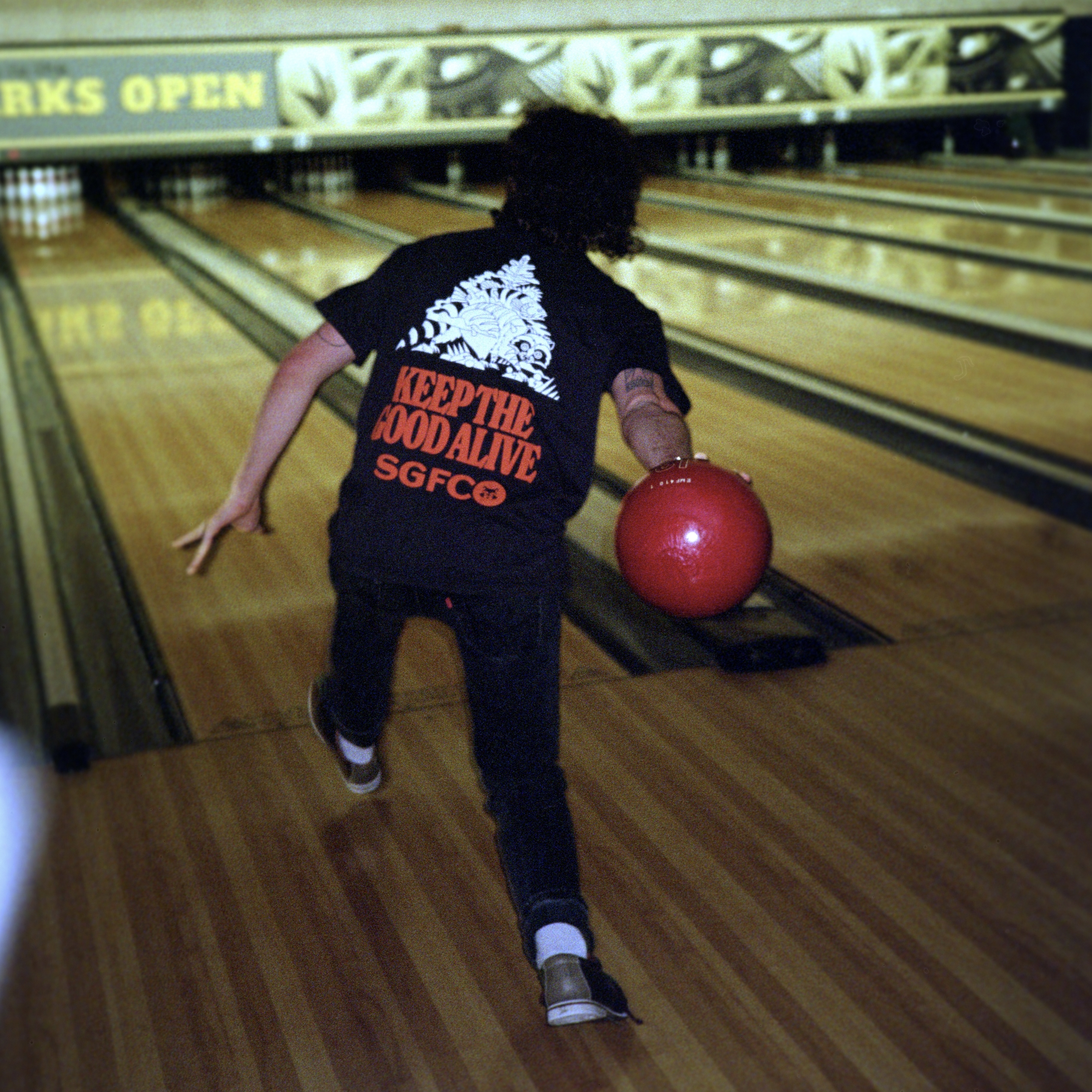 A bowler prepares to roll a red ball down a bowling lane