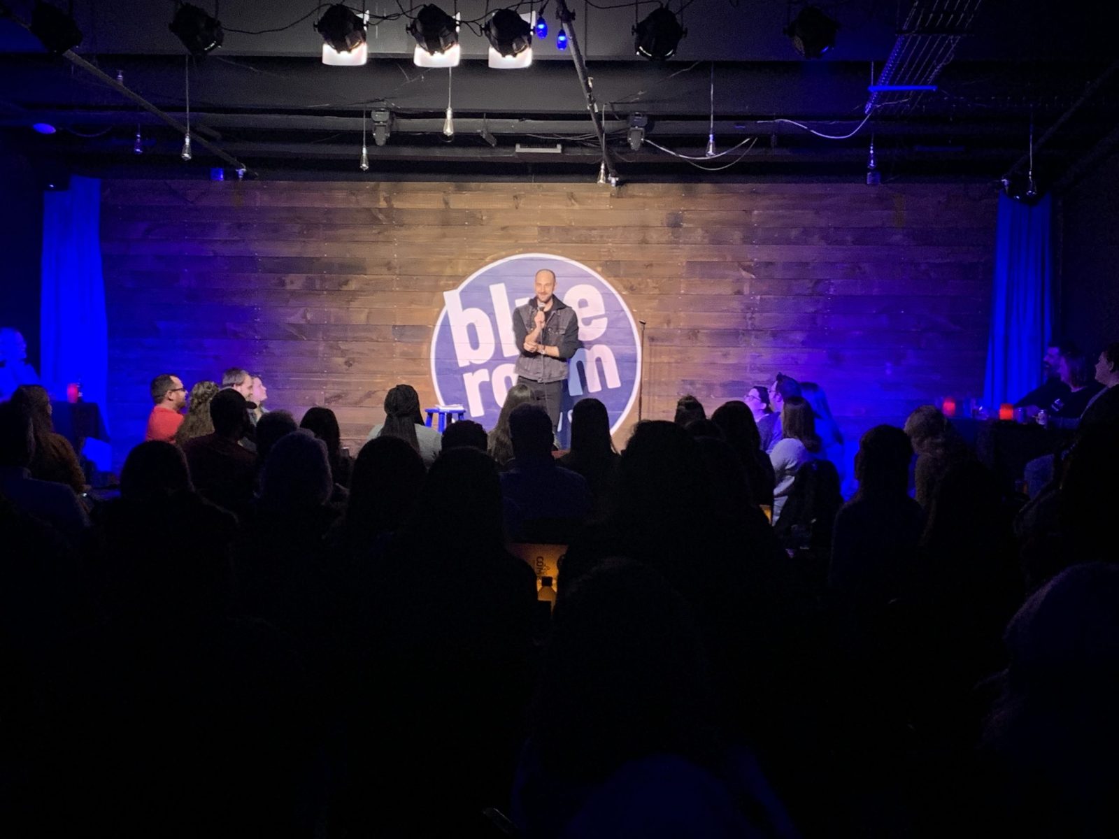 A comedian stands on stage at a club, telling jokes