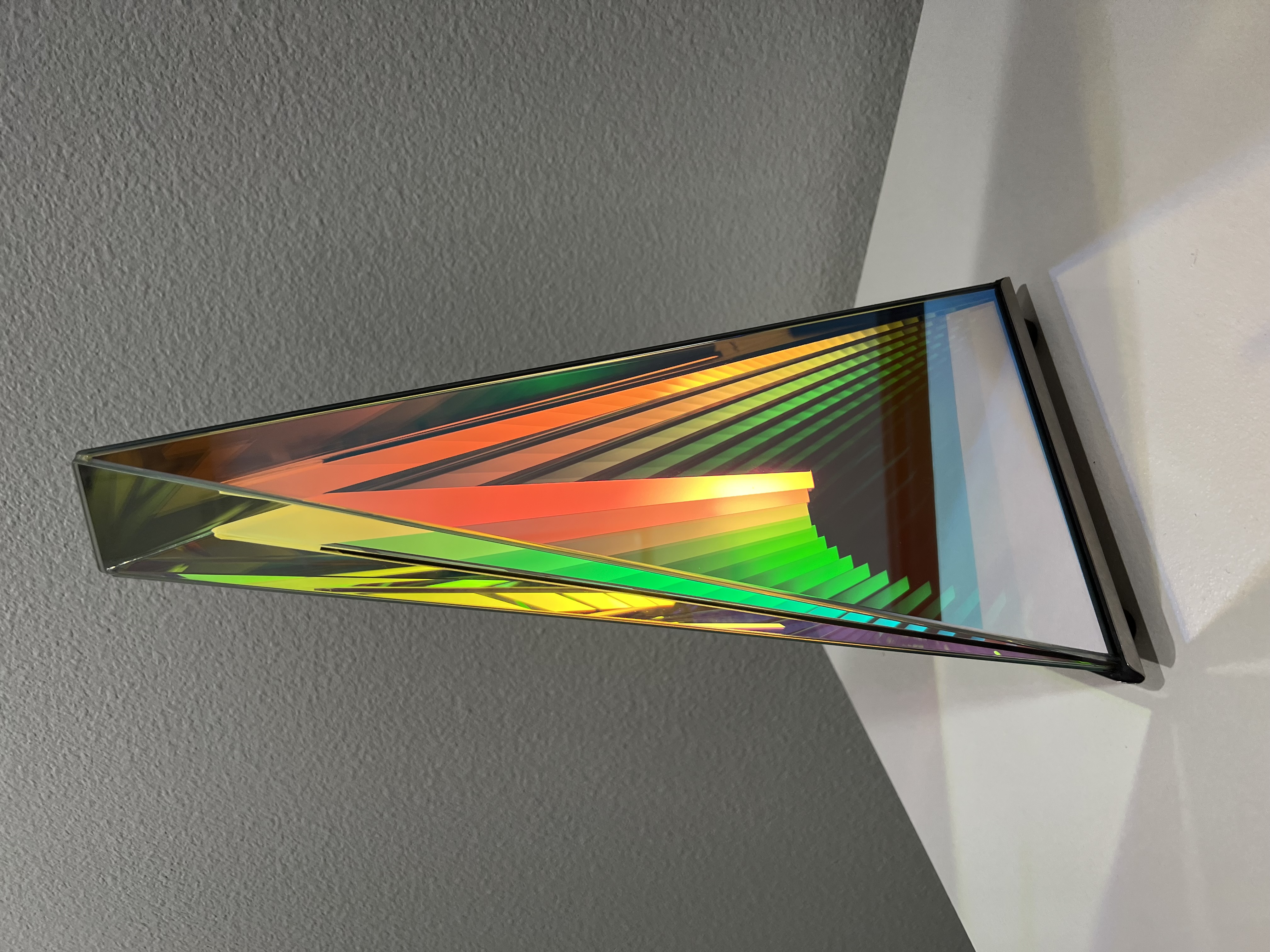 A glass pyramid sculpture with red, orange and green light rays on the inside