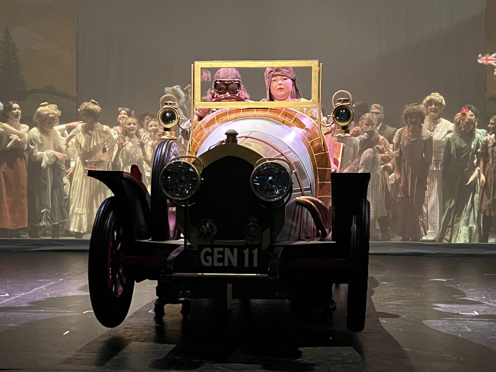 Two children sit inside a car on stage at a theater