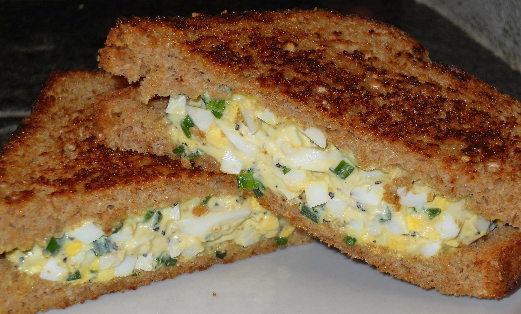An egg salad sandwich sits on a white plate