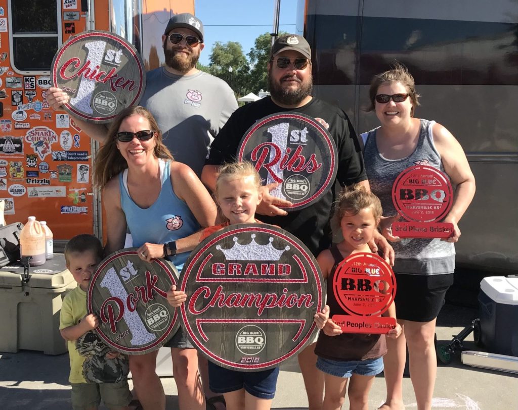 A family holds up trophies won at a barbecue cooking competition