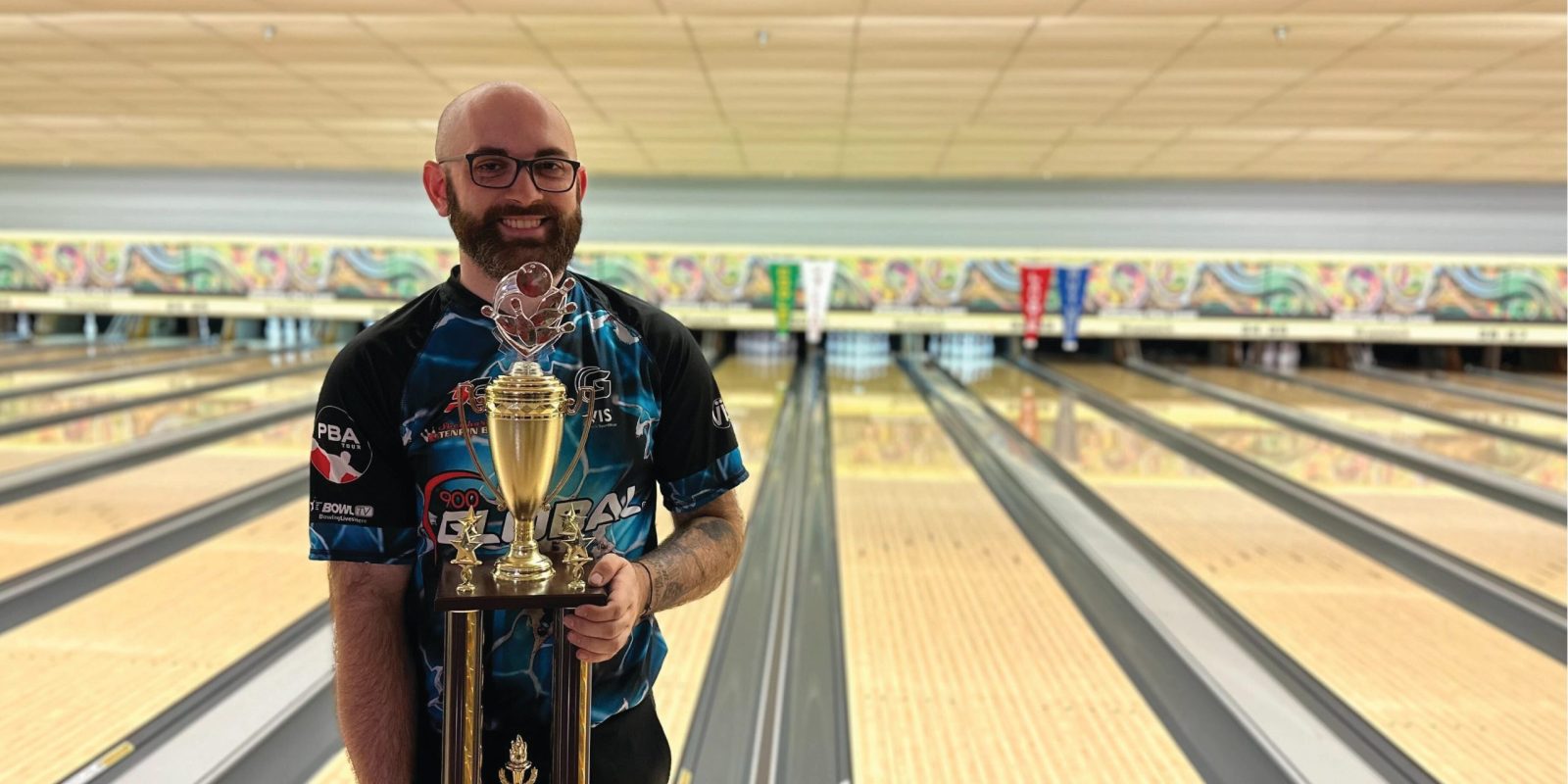 A man holds a trophy while standing next to bowling lanes