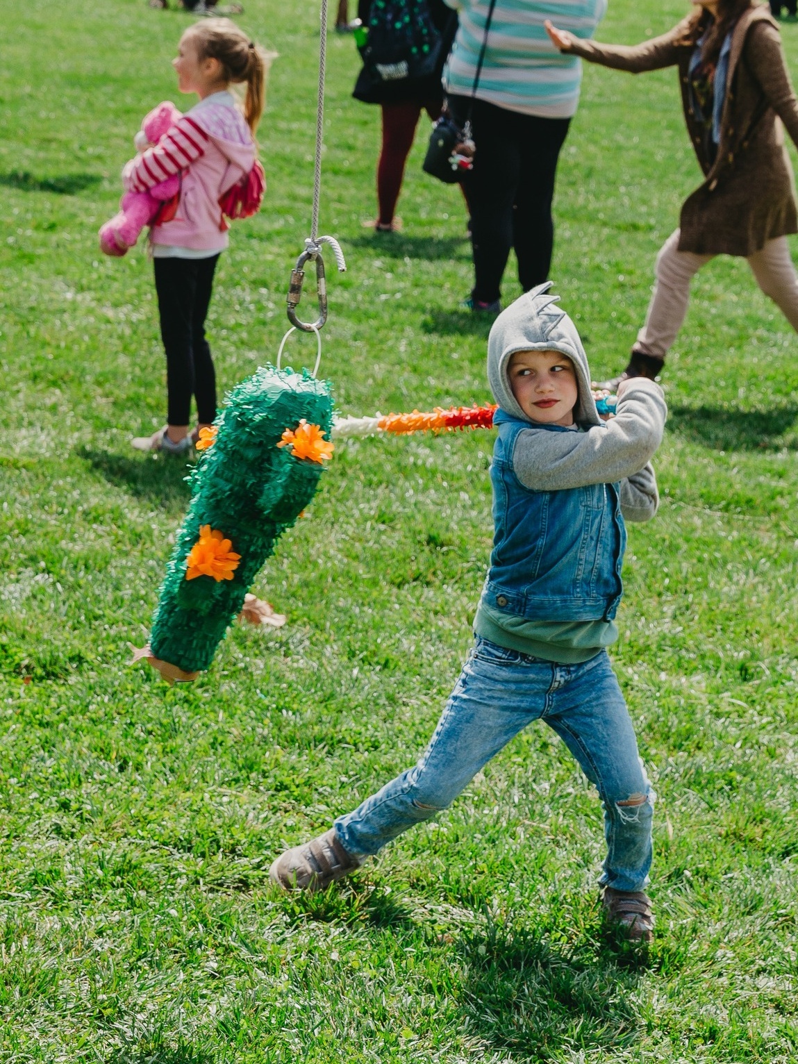 A child in a hooded sweatshirt prepares to swing a stick at a pinata