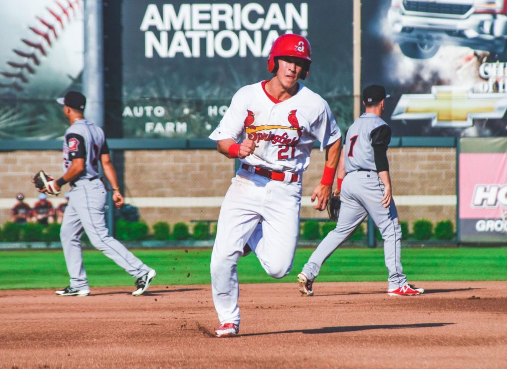 A baseball player in a white uniform and red helmet runs to third base