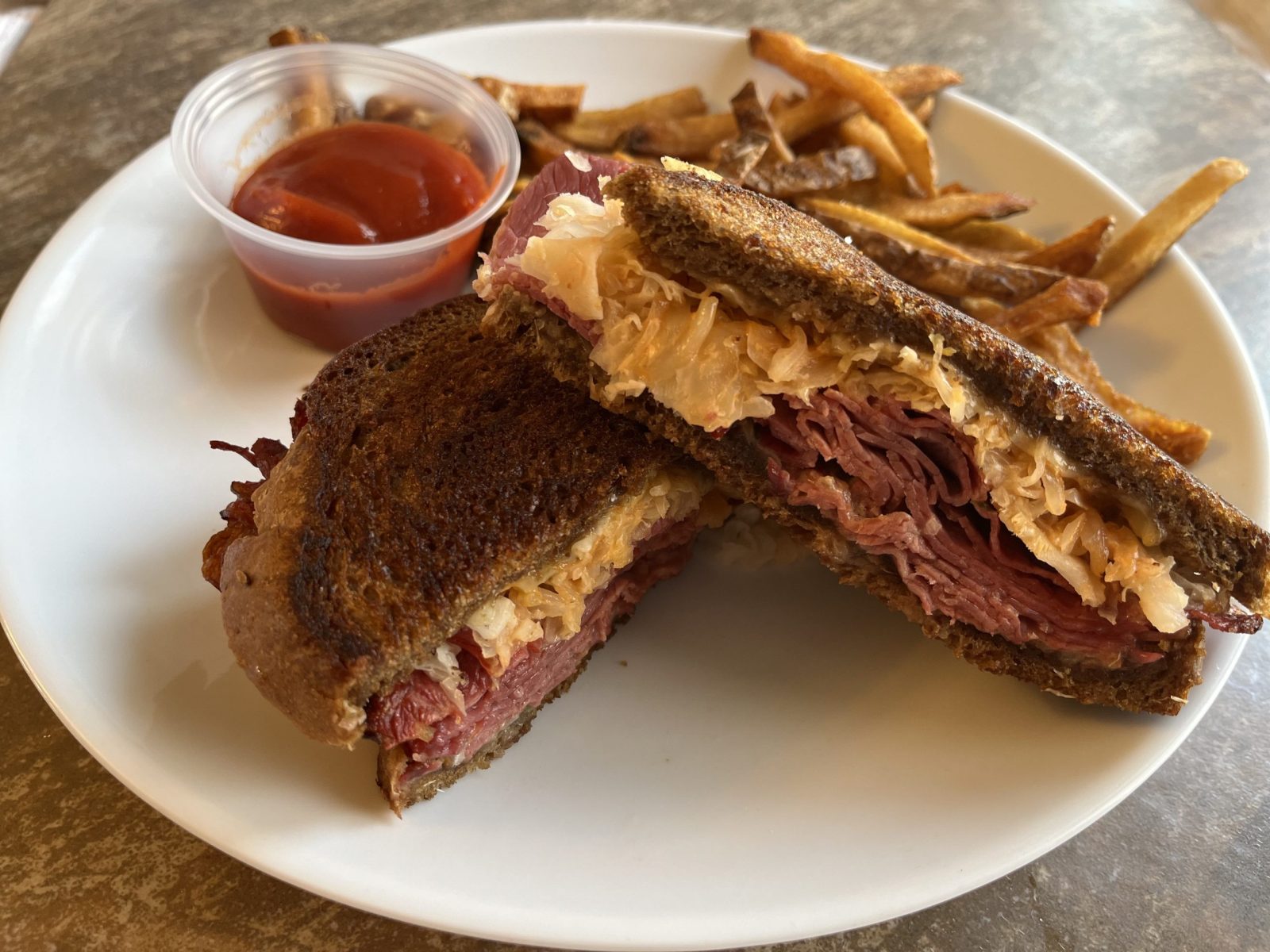 A Reuben sandwich and french fires sit on a white plate