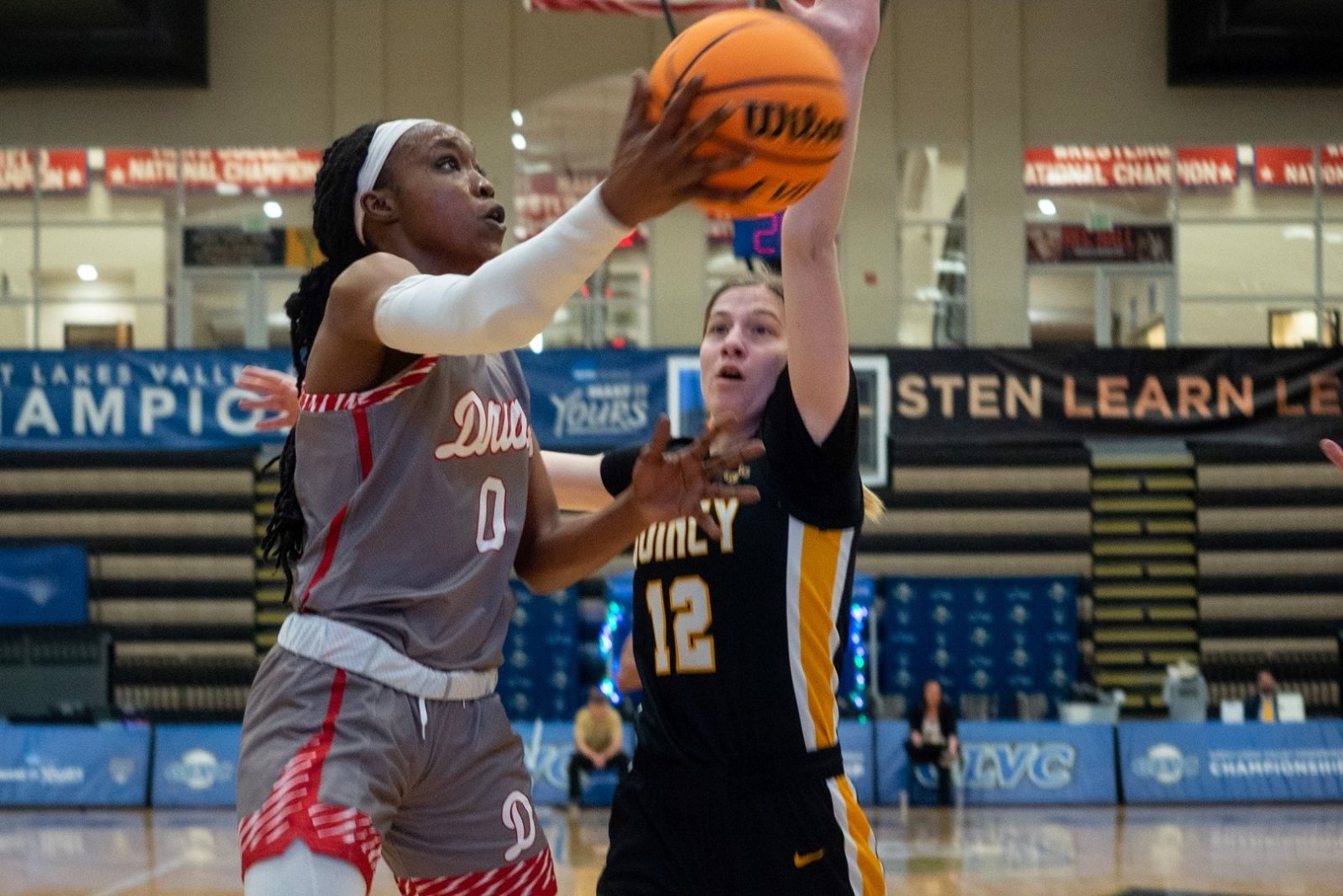 A basketball player shoots a layup as an opponent guards her