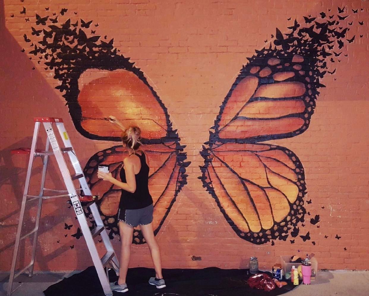 A woman paints a mural on an outdoor wall