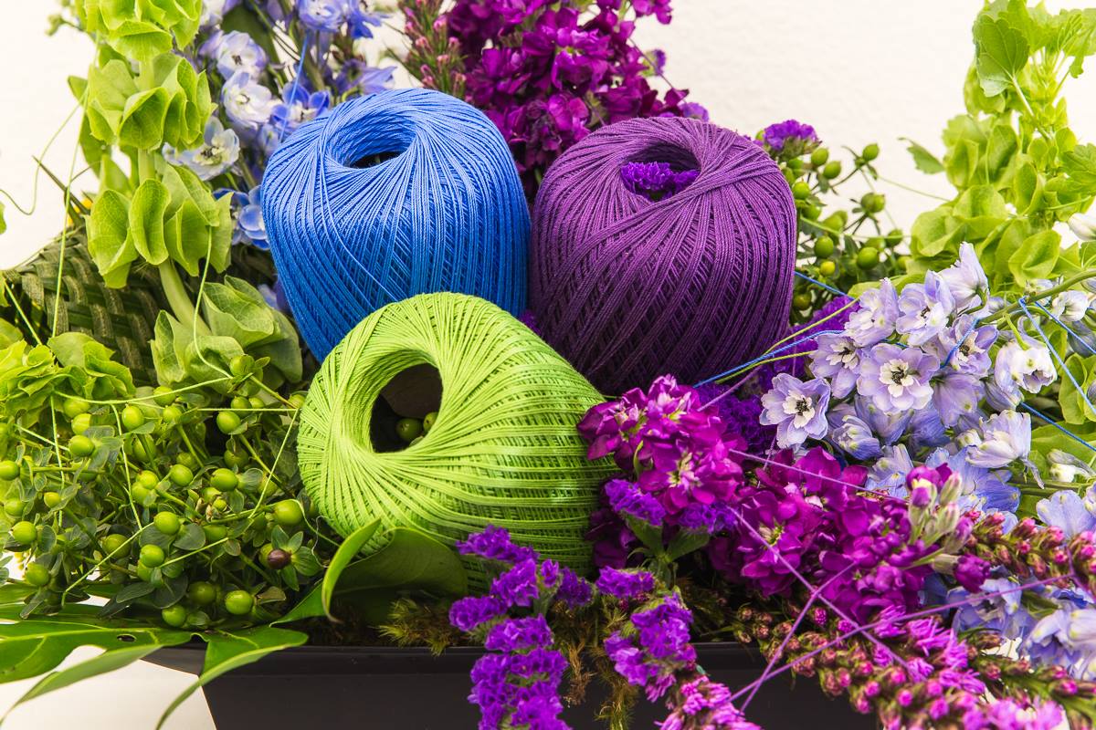 Three spools of thread — one blue, one purple and one green — rest on a bed of flowers