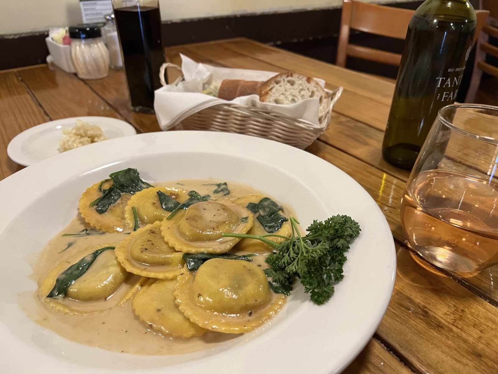 A plate of ravioli sits on a table, surrounded by bread and wine