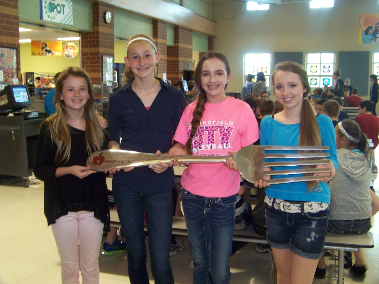 Four middle school students hold a giant silver fork