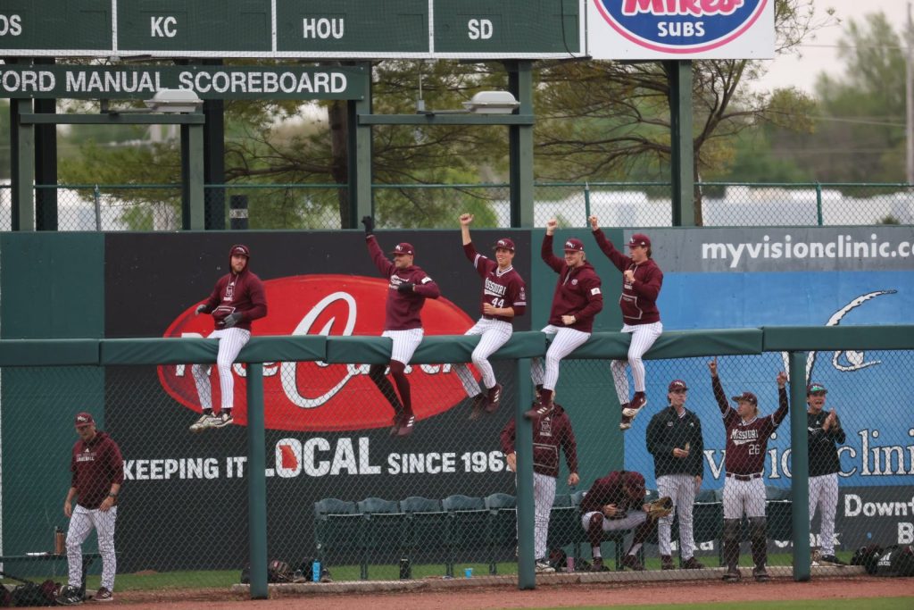 Baseball players sit on the bullpen fence, celebrating a home run