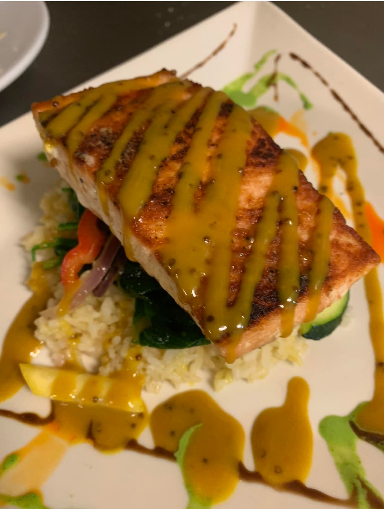 A salmon filet sits on a plate, with basmati rice and sauteed vegetabales