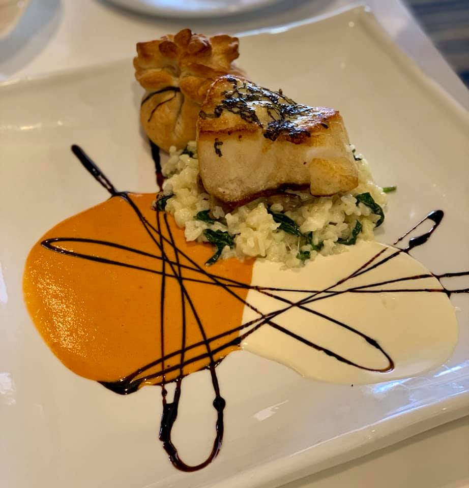 A Chilean sea bass filet sits on a white plate, with a puff pastry and butter sauce