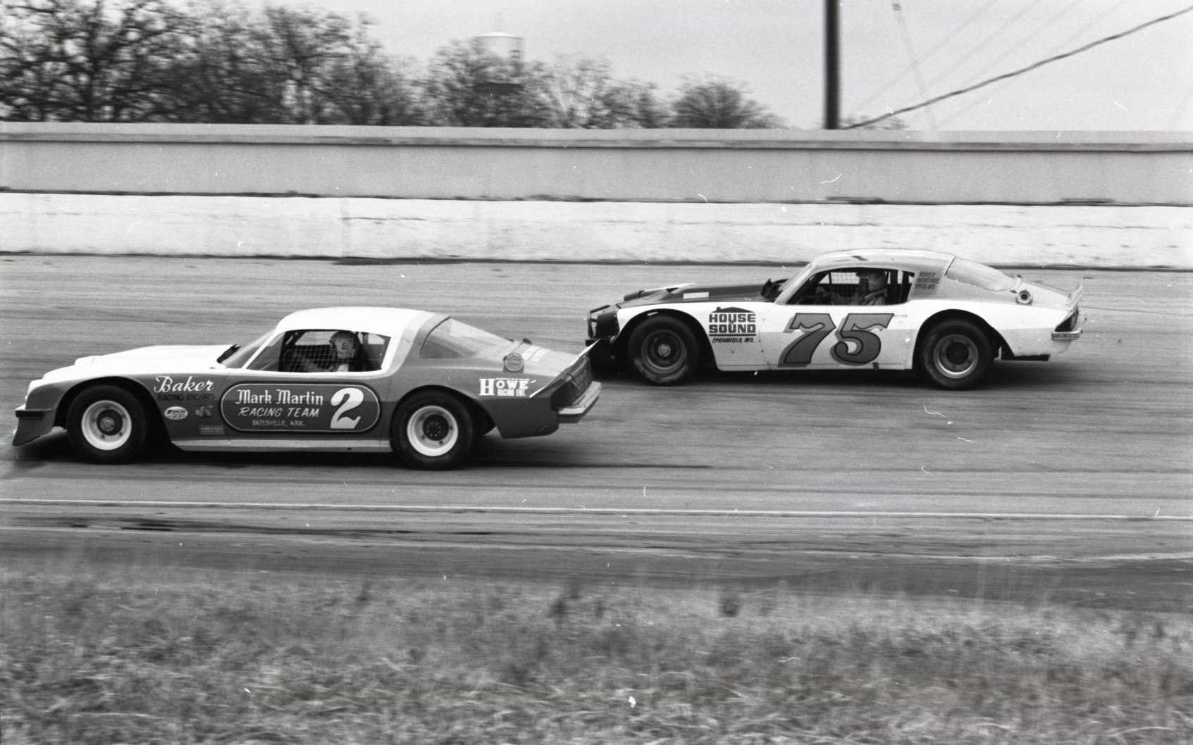 Black-and-white photo of two race cars speeding down a track