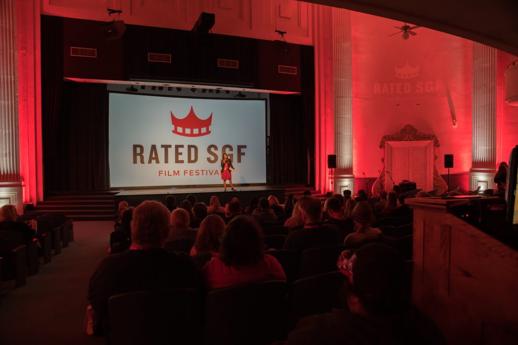 A person stands on a stage in front of a backdrop that reads "Rated SGF"