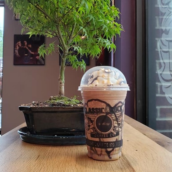 A frappe in a Classic Rock Coffee cup sits next to a bonsai tree
