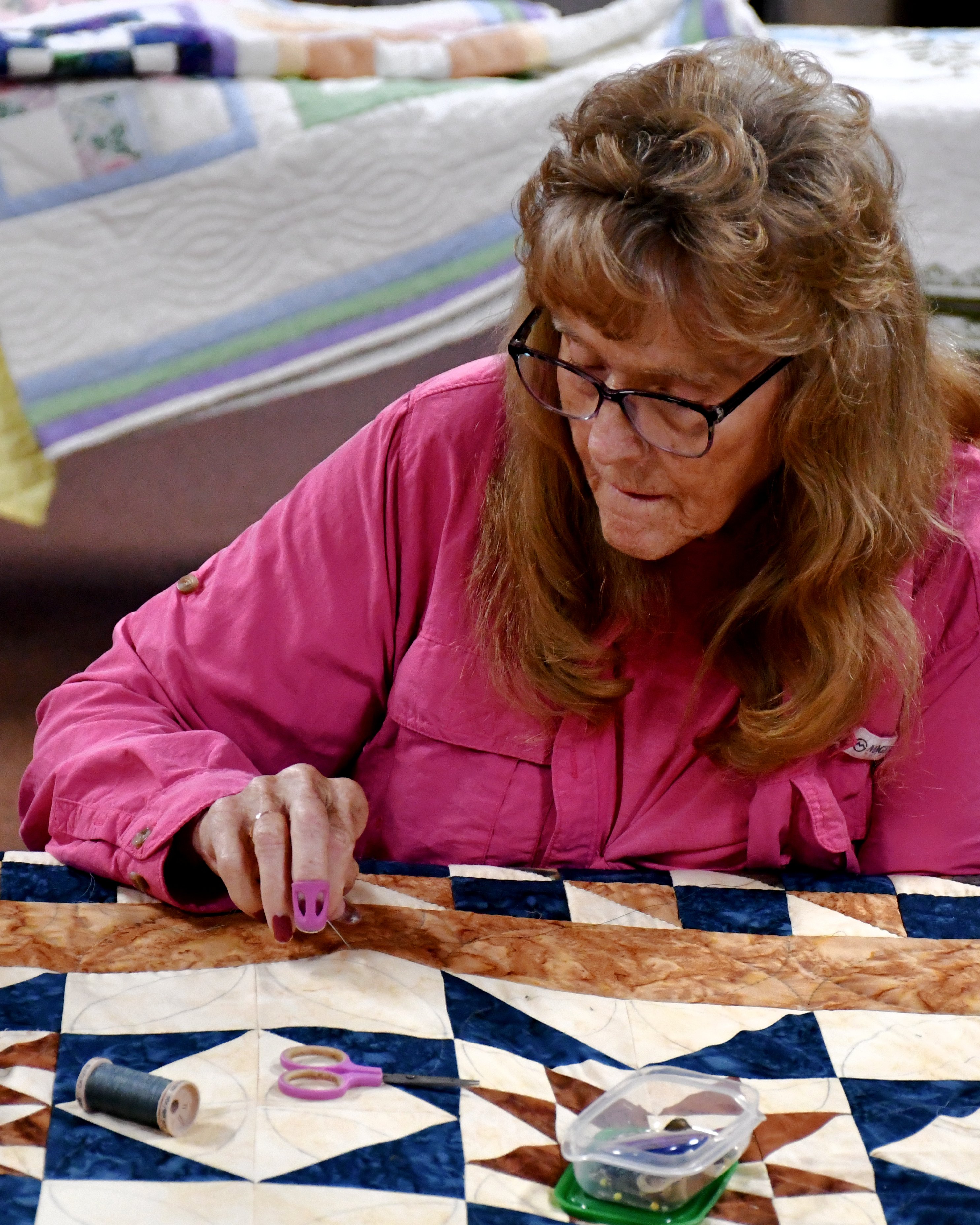A woman in a pink shirt works on a quilt