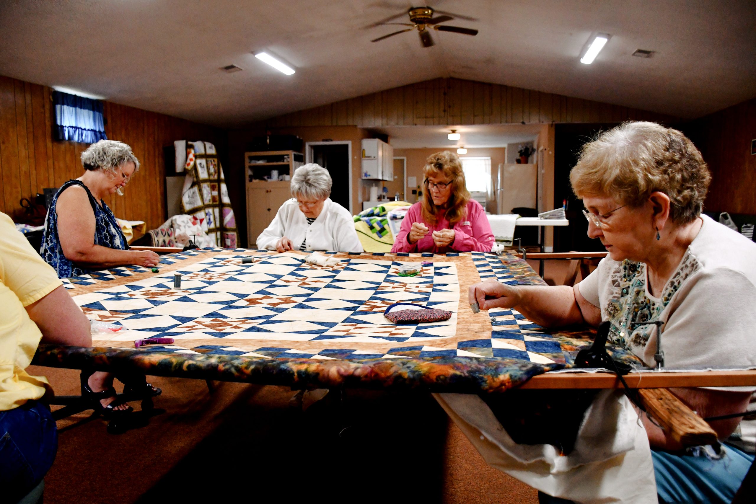 A group of women sit around a large table, working on a quilt