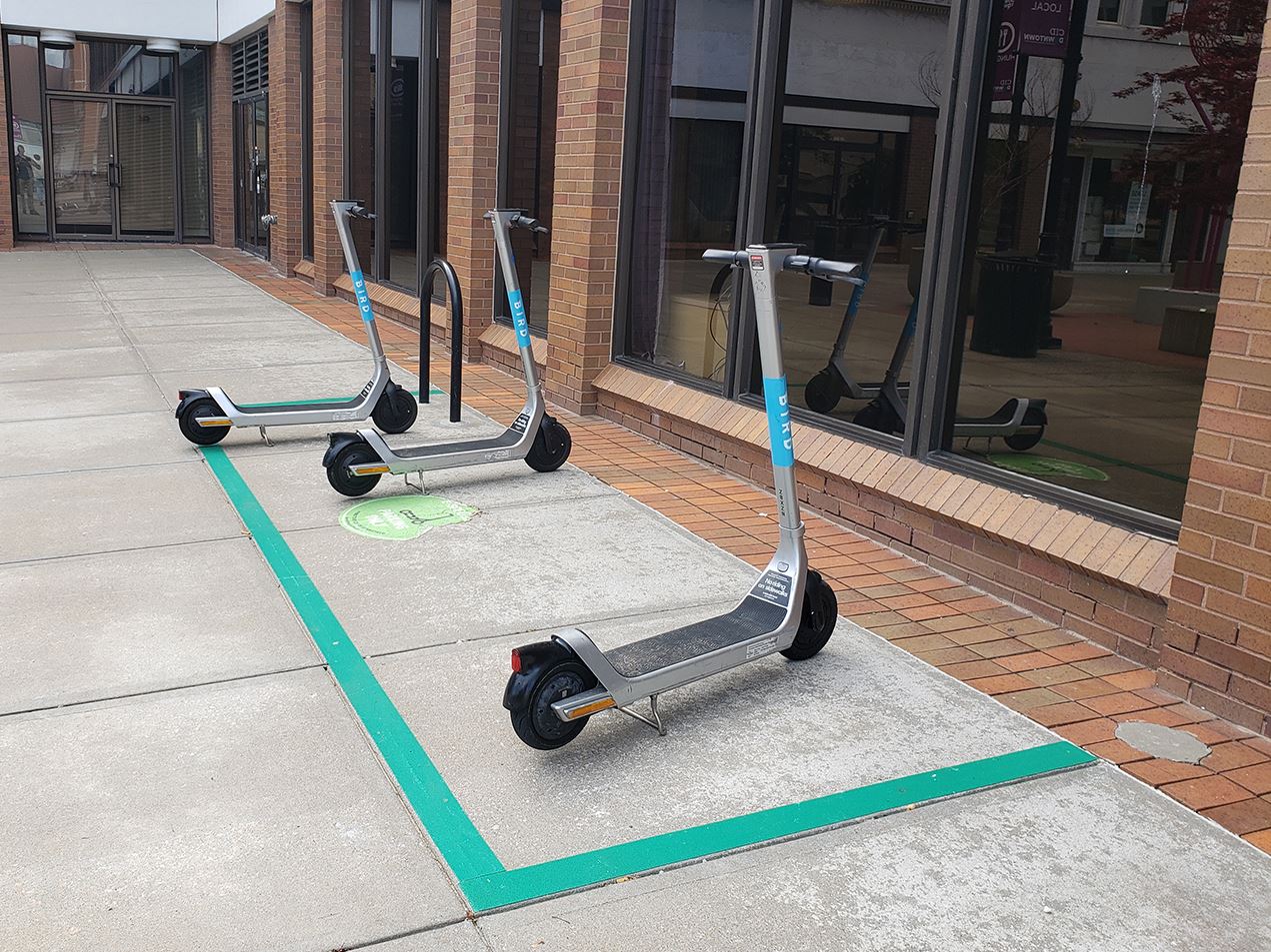 Three Bird electric scooters are parked in a "corral," a taped off area on a sidewalk in downtown Springfield.