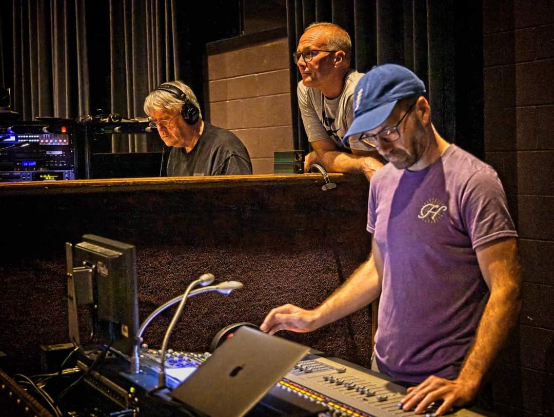 Three men stand in the production booth during a concert