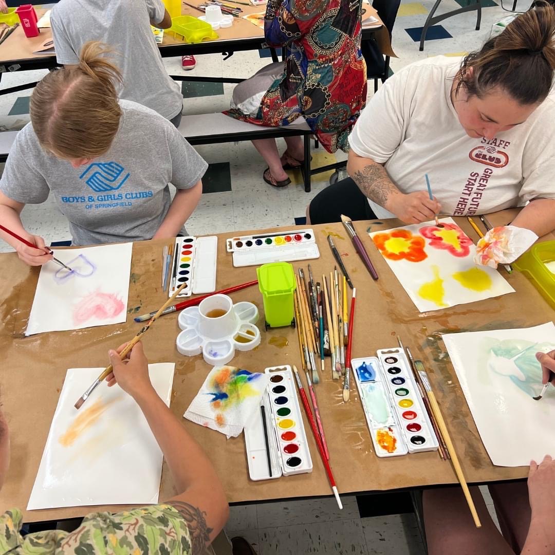 Four adults sit around a classroom table, painting butterflies