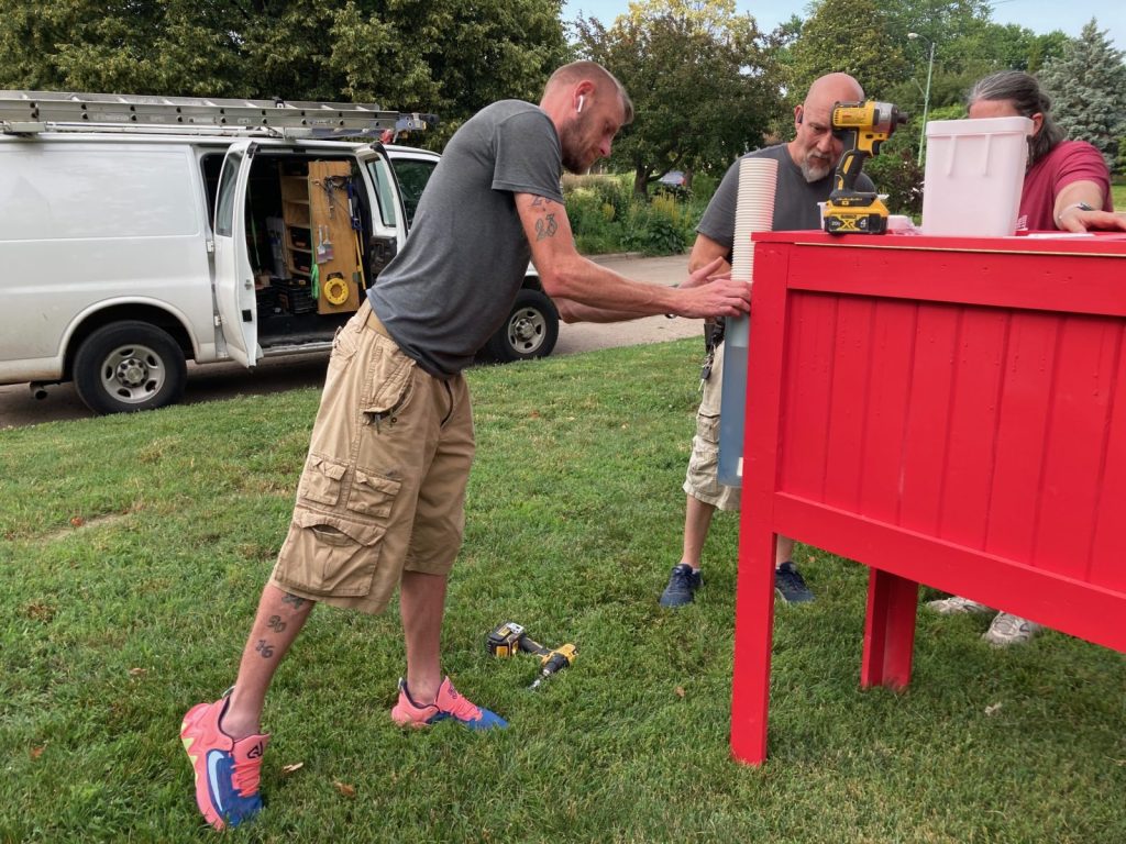 Connecting Grounds Lived Experience Cohort member Charles Brink (left) helps Bob Love install a paper cup dispenser on a water refill station near National Avenue Christian Church