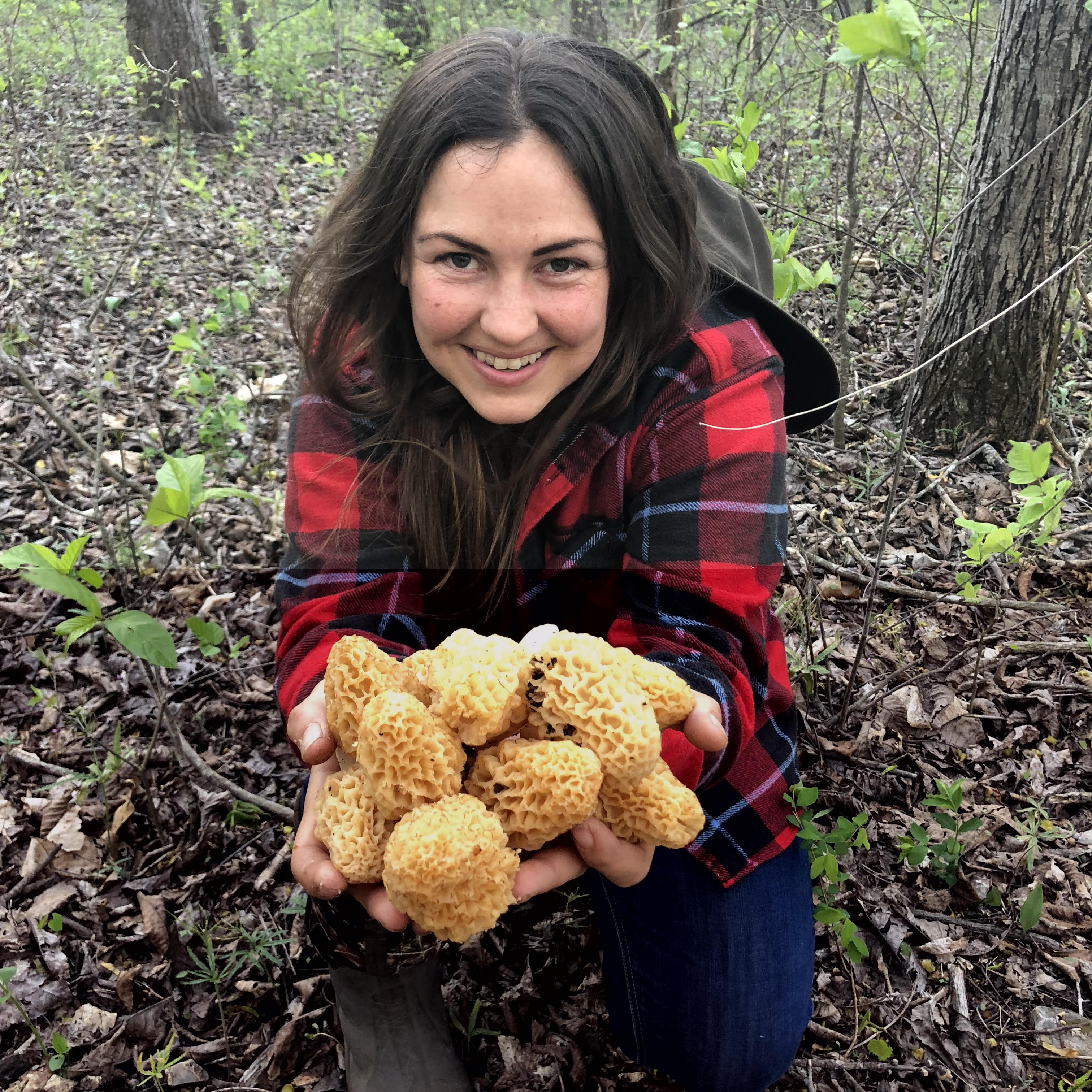 A woman in a red plaid jacket holds up morel mushrooms