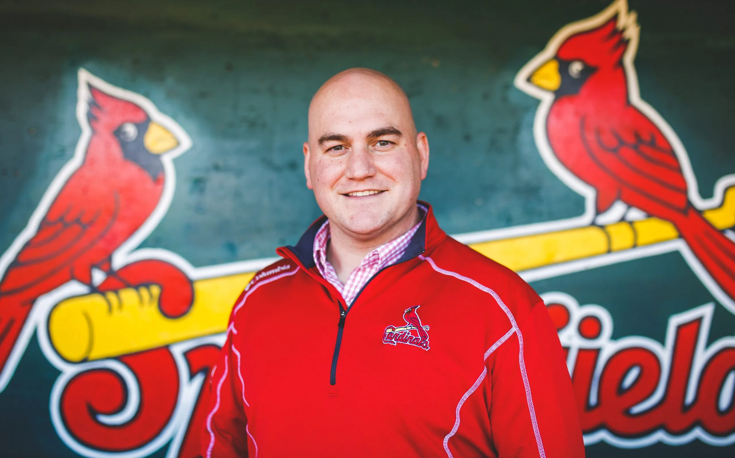 A man in a red jacket poses in front of a Springfield Cardinals logo