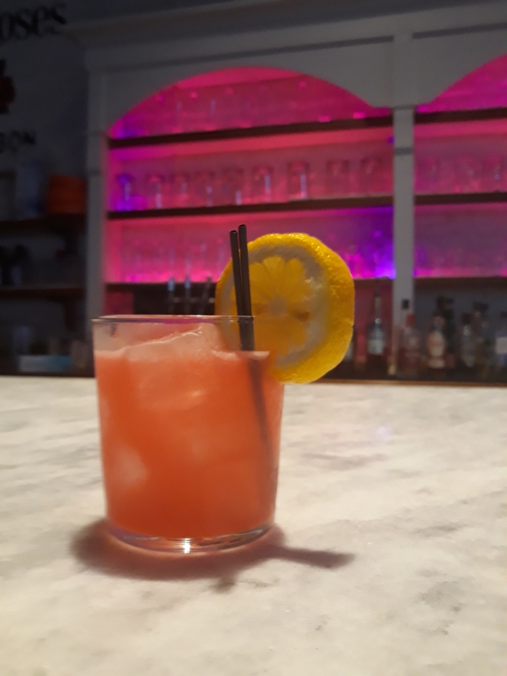 A pink-hued mocktail sits on a marble-top bar