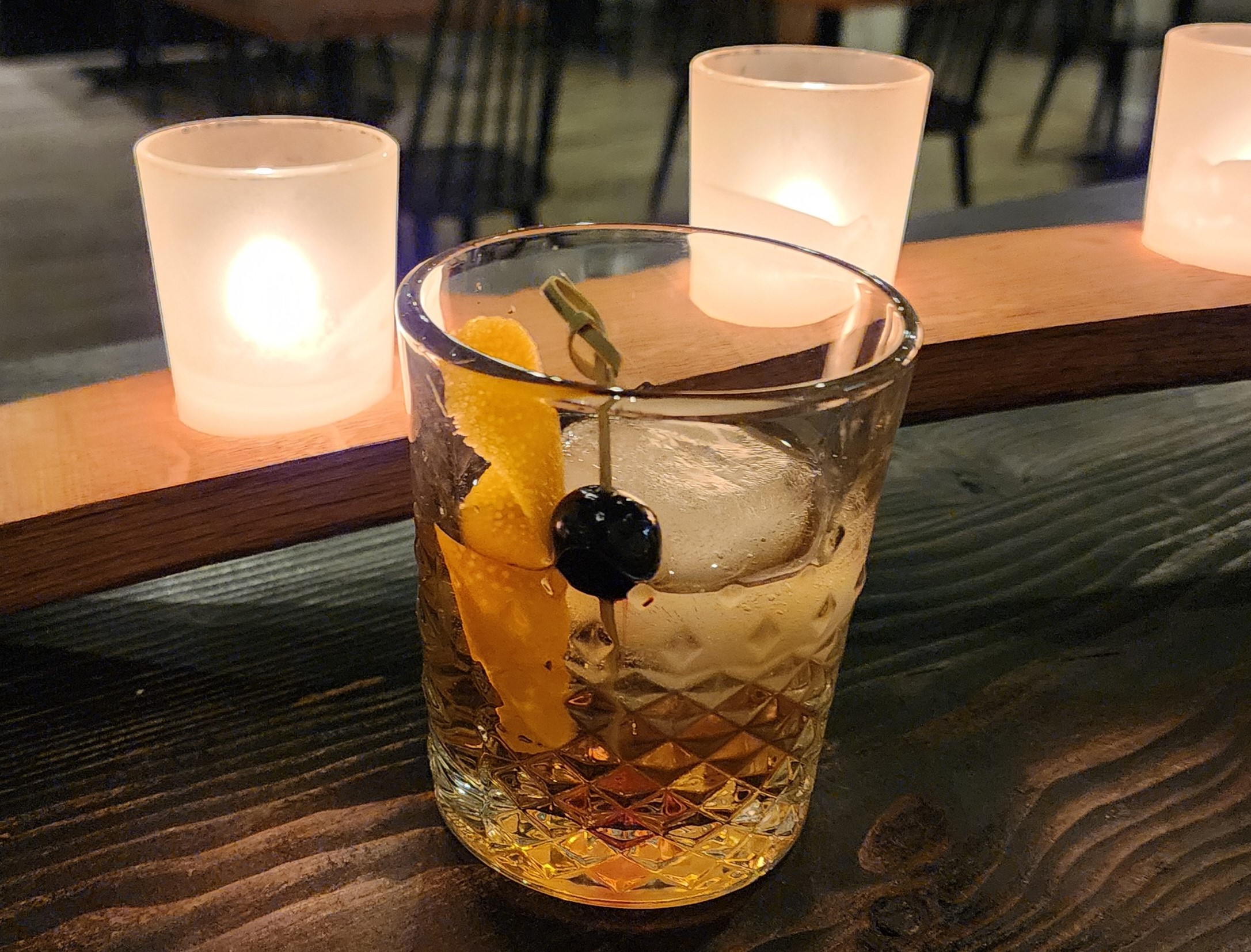 A cocktail sits on a bar, with three lit candles behind it